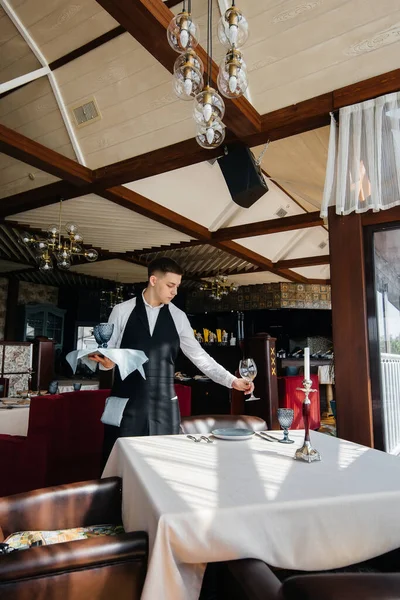 一位穿着时髦制服的年轻男服务员在一家漂亮的美食家餐厅里为餐桌服务 最高层次的餐厅活动 — 图库照片