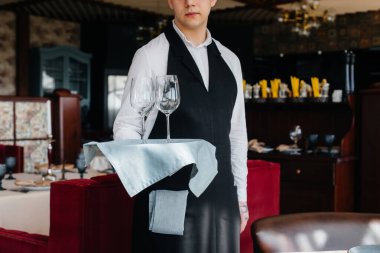 Şık üniformalı genç bir garson, güzel bir gurme restoranında masanın yanındaki tepside gözlükleriyle ayakta duruyor. Restoran faaliyetleri, en üst düzeyde..
