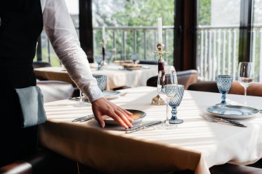 Şık üniformalı genç bir garson güzel bir gurme restoranında masaya servis yapmakla meşgul. Restoran faaliyetleri, en üst düzeyde..