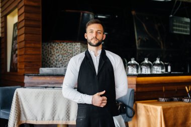 Sakallı genç bir garson önlüğünü giyer ve güzel bir restoranda çalışmaya hazırlanır..