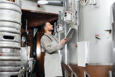 Genç sakallı bir bira üreticisi demleme sırasında sensör okumalarını izliyor. Bira yapıyorum..