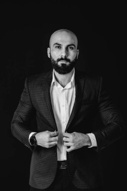 Beyaz gömlekli ve ceketli genç sakallı bir adam siyah arka planda duruyor. Siyah ve beyaz.