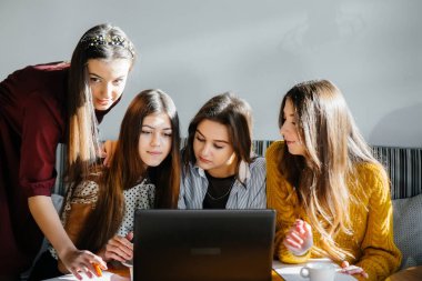 Bir grup genç kız ofiste oturup bilgisayar başında çalışıyor. İletişim ve eğitim çevrimiçi.
