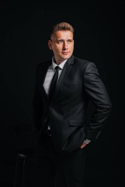 Siyah takım elbiseli ve siyah arka planda gülümseyen yakışıklı bir genç. Temizlen, hazırlan..