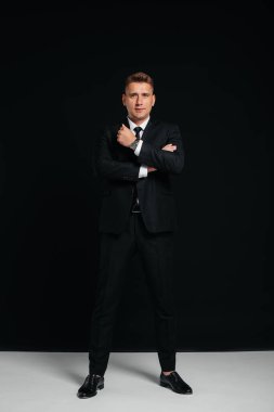 Siyah takım elbiseli yakışıklı bir genç siyah arka planda poz veriyor. Şık bir iş adamı. Büyük bir iş adamı..