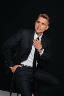 Siyah takım elbiseli ve siyah arka planda gülümseyen yakışıklı bir genç. Temizlen, hazırlan..