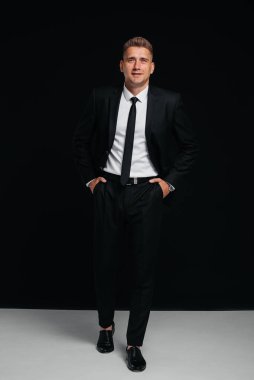 Siyah takım elbiseli yakışıklı bir genç siyah arka planda poz veriyor. Şık bir iş adamı. Büyük bir iş adamı..