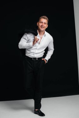 Yakışıklı genç bir adam ceketini çıkarıp siyah arka planda poz vererek gülüyor. Şık bir iş adamı. Büyük bir iş adamı..