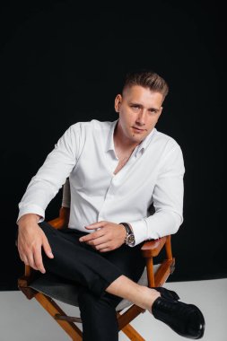Beyaz gömlekli şık bir genç adam siyah arka planda yönetmen koltuğunda oturuyor. Yakışıklı, karizmatik bir iş adamı..