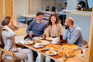 Bir grup neşeli genç arkadaş bir kafede oturmuş konuşuyor ve pizza yiyorlar. Pizzacıda öğle yemeği..