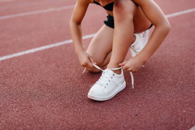 Gün batımında stadyumda koşmadan önce küçük bir kız ayakkabı bağcıklarını bağlamak için oturdu. Çocuk sporu ve sağlıklı bir yaşam tarzı..
