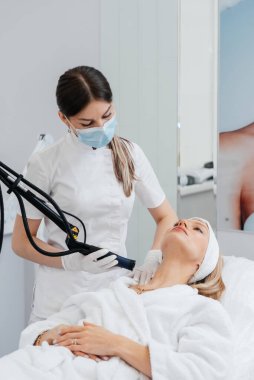 Genç bir kız güzellik salonunda boynun derisi için karbon soyuyorlar. Lazer darbeleri deriyi temizler. Donanım kozmetolojisi. Fototermoliz süreci, deriyi ısıtır..