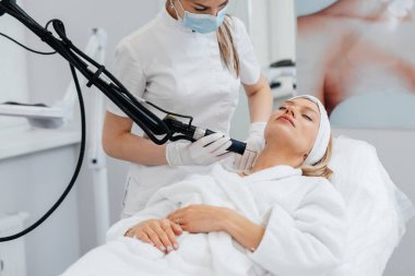 Genç bir kız güzellik salonunda boynun derisi için karbon soyuyorlar. Lazer darbeleri deriyi temizler. Donanım kozmetolojisi. Fototermoliz süreci, deriyi ısıtır..