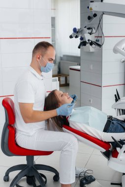 Genç bir dişçi uzmanı modern beyaz dişçilikte güzel bir kadının dişlerini muayene eder ve tedavi eder. Diş protezi, tedavi ve diş beyazlatma. Modern dişçilik.