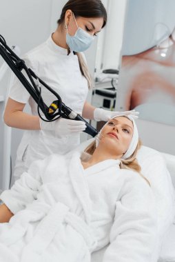 Genç bir kız güzellik salonunda yüzünün derisi için kömür soyuyordu. Lazer darbeleri deriyi temizler. Donanım kozmetolojisi. Fototermoliz süreci, deriyi ısıtır..