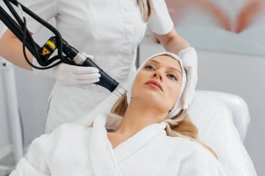 Genç bir kız güzellik salonunda yüzünün derisi için kömür soyuyordu. Lazer darbeleri deriyi temizler. Donanım kozmetolojisi. Fototermoliz süreci, deriyi ısıtır..