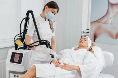 Genç bir kız güzellik salonunda ellerinin derisi için karbon soyuluyor. Lazer darbeleri deriyi temizler. Donanım kozmetolojisi. Fototermoliz süreci, deriyi ısıtır..