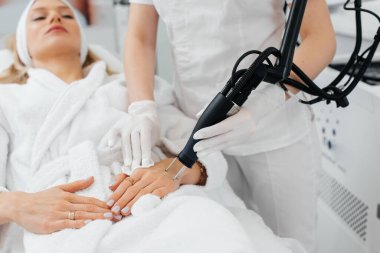 Genç bir kız güzellik salonunda ellerinin derisi için karbon soyuluyor. Lazer darbeleri deriyi temizler. Donanım kozmetolojisi. Fototermoliz süreci, deriyi ısıtır..