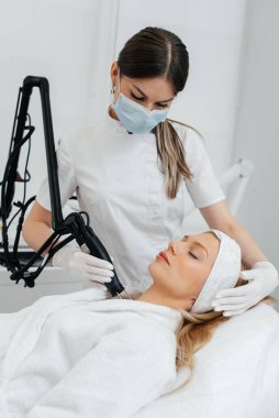 Genç bir kız güzellik salonunda boynun derisi için karbon soyuyorlar. Lazer darbeleri deriyi temizler. Donanım kozmetolojisi. Fototermoliz süreci, deriyi ısıtır..