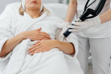 Genç bir kız güzellik salonunda ellerinin derisi için karbon soyuluyor. Lazer darbeleri deriyi temizler. Donanım kozmetolojisi. Fototermoliz süreci, deriyi ısıtır..
