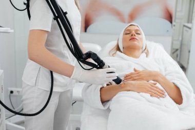 Genç bir kız güzellik salonunda ellerinin derisi için karbon soyuluyor. Lazer darbeleri deriyi temizler. Donanım kozmetolojisi. Fototermoliz süreci, deriyi ısıtır..