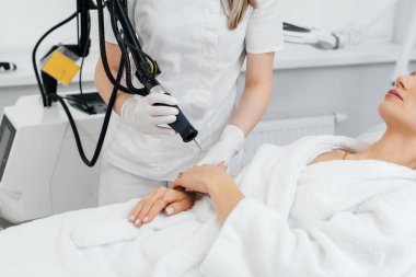 Genç bir kız güzellik salonunda ellerinin derisi için karbon soyuluyor. Lazer darbeleri deriyi temizler. Donanım kozmetolojisi. Fototermoliz süreci, deriyi ısıtır..