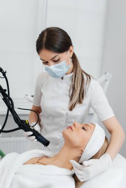 Genç bir kız güzellik salonunda boynun derisi için karbon soyuyorlar. Lazer darbeleri deriyi temizler. Donanım kozmetolojisi. Fototermoliz süreci, deriyi ısıtır..