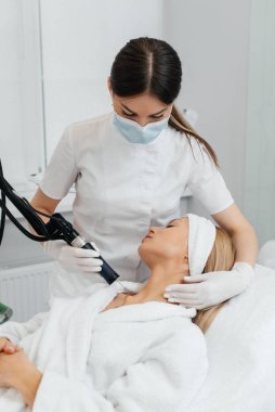 Genç bir kız güzellik salonunda boynun derisi için karbon soyuyorlar. Lazer darbeleri deriyi temizler. Donanım kozmetolojisi. Fototermoliz süreci, deriyi ısıtır..