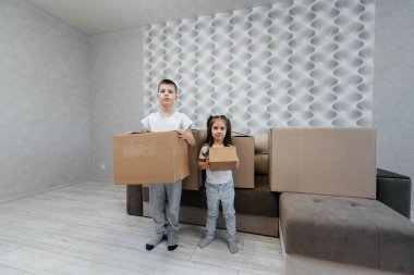 Erkek ve kız kardeşler karton kutuların ve kanepenin arka planında yeni bir daireye taşınıp eğleniyorlar. Gayrimenkul alımı. Ev partisi, teslimat..