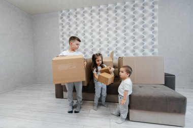 Erkek ve kız kardeşler karton kutuların ve kanepenin arka planında yeni bir daireye taşınıp eğleniyorlar. Gayrimenkul alımı. Ev partisi, teslimat..