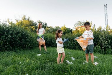 Gün batımında bir grup yetişkin ve çocuk parkta çöp toplamakla meşgul. Çevresel bakım, atık geri dönüşümü. Çöp ayıklama.
