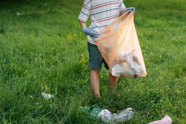 Gün batımında yedi yaşında bir çocuk parkta çöp toplamakla meşgul. Çevre bakımı, geri dönüşüm.