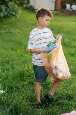 Gün batımında yedi yaşında bir çocuk parkta çöp toplamakla meşgul. Çevre bakımı, geri dönüşüm.