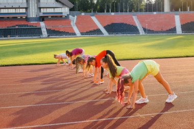 Büyük bir grup kız gün batımında stadyumda koşmadan önce hazırlandılar. Sağlıklı bir yaşam tarzı.