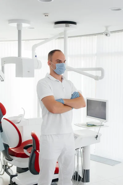 Młody Dentysta Masce Stoi Pobliżu Czerwonego Krzesła Dentystycznego Uśmiecha Się — Zdjęcie stockowe