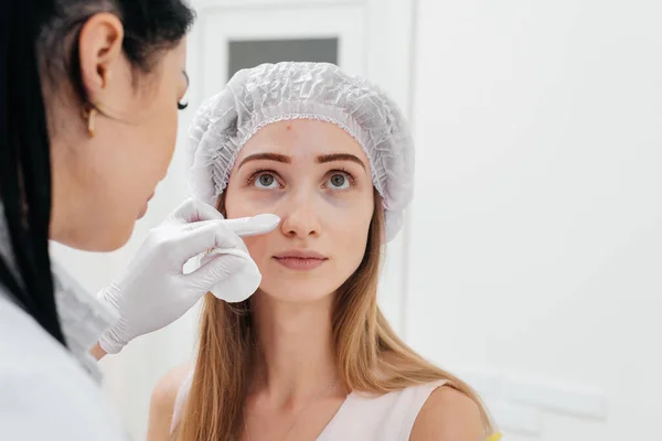 美容師は若い美少女のために眼の周りの鼻の毛細管とメソセラピーを埋める手順の後 患者の顔を拭く 近代化粧品 — ストック写真