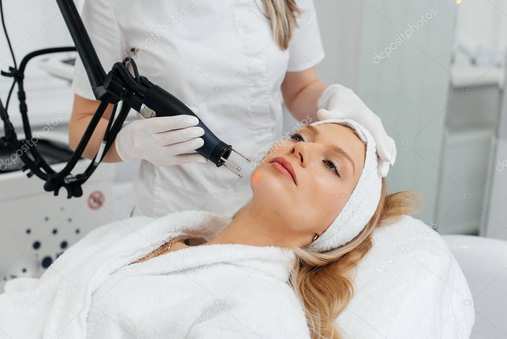 A young girl gets a charcoal peeling for the skin of the face in a beauty salon. Laser pulses cleanse the skin. Hardware cosmetology. The process of photothermolysis, warming the skin.