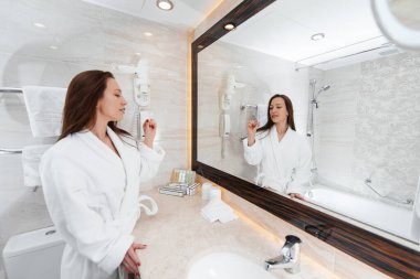Genç güzel bir kız güzel beyaz bir banyoda dişlerini fırçalıyor. Otelde taze bir günaydın. Dinlen ve seyahat et. Otel eğlencesi ve turizm..