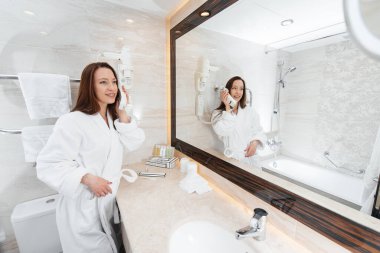 Güzel beyaz bir banyoda genç ve güzel bir kız telefonda konuşuyor. Otelde taze bir günaydın. Dinlen ve seyahat et. Otel eğlencesi ve turizm..