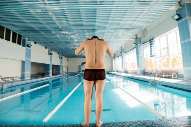 Genç bir adam modern bir yüzme havuzunda çalışmaya hazırlanıyor. Eğitim ve spor gelişimi. Yarışmalara hazırlık ve sağlıklı bir yaşam tarzı. Su tedavileri ve sağlıklı bir yaşam tarzı..