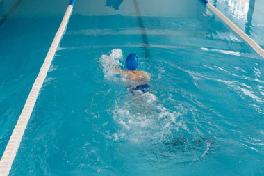 Sekiz yaşında küçük bir çocuk modern bir yüzme havuzunda yüzmeyi öğreniyor. Çocuk sporlarının gelişimi. Sağlıklı ebeveynlik ve çocuk sporlarının tanıtımı.