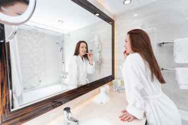 Genç güzel bir kız güzel beyaz bir banyoda dişlerini fırçalıyor. Otelde taze bir günaydın. Dinlen ve seyahat et. Otel eğlencesi ve turizm..
