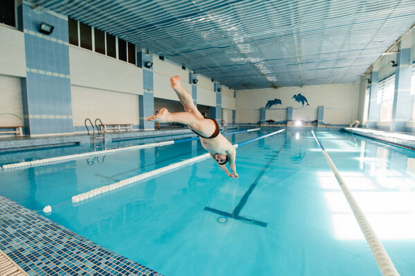A young man dives and jumps into the water of a modern swimming pool. Training and sports development. Preparation for competitions, and a healthy lifestyle. Water treatments and a healthy lifestyle.