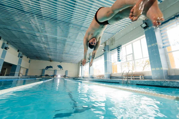 A young man dives and jumps into the water of a modern swimming pool. Training and sports development. Preparation for competitions, and a healthy lifestyle. Water treatments and a healthy lifestyle.