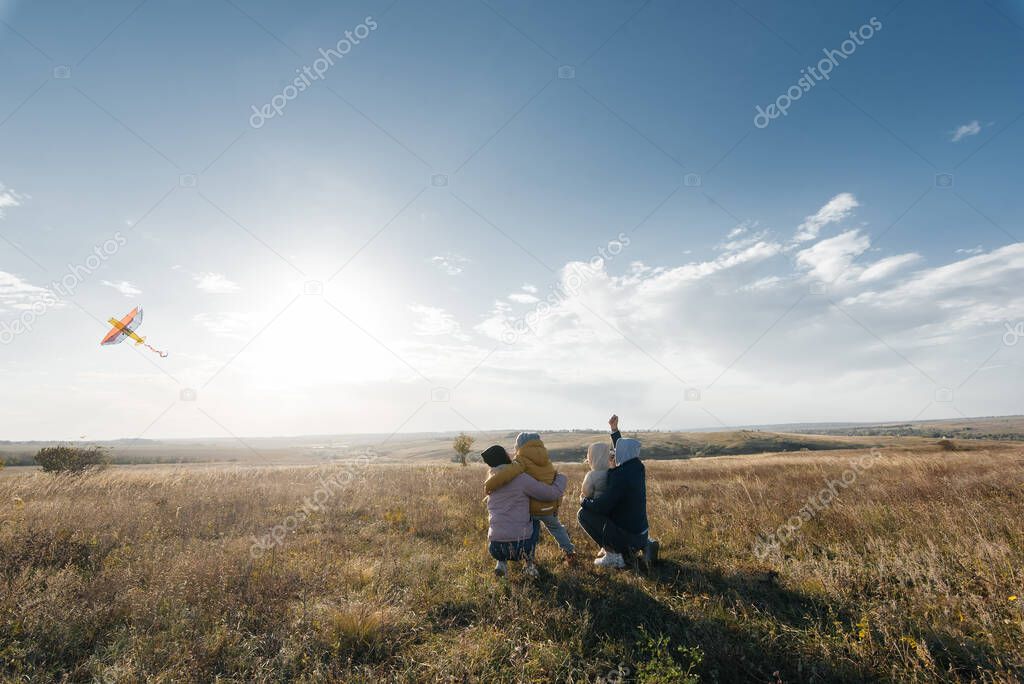 A happy family with children flies a kite and spends time together outdoors in a nature reserve. Happy childhood and family holidays. Freedom and space.