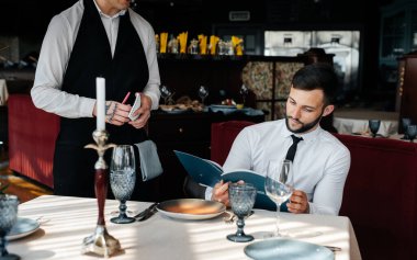 İyi bir restoranda genç bir işadamı menüyü inceler ve şık önlüklü genç bir garsona sipariş verir. Müşteri hizmetleri. Restorandaki masa servisi..