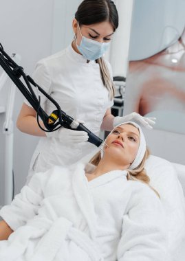 Genç bir kız güzellik salonunda yüzünün derisi için kömür soyuyordu. Lazer darbeleri deriyi temizler. Donanım kozmetolojisi. Fototermoliz süreci, deriyi ısıtır..