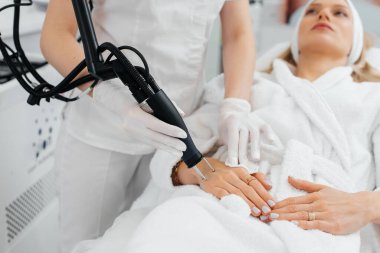 Genç bir kız güzellik salonunda ellerinin derisi için karbon soyuluyor. Lazer darbeleri deriyi temizler. Donanım kozmetolojisi. Fototermoliz süreci, deriyi ısıtır..