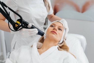 Genç bir kız güzellik salonunda yüzünün derisi için kömür soyuyordu. Lazer darbeleri deriyi temizler. Donanım kozmetolojisi. Fototermoliz süreci, deriyi ısıtır..