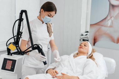 Genç bir kız güzellik salonunda ellerinin derisi için karbon soyuluyor. Lazer darbeleri deriyi temizler. Donanım kozmetolojisi. Fototermoliz süreci, deriyi ısıtır..